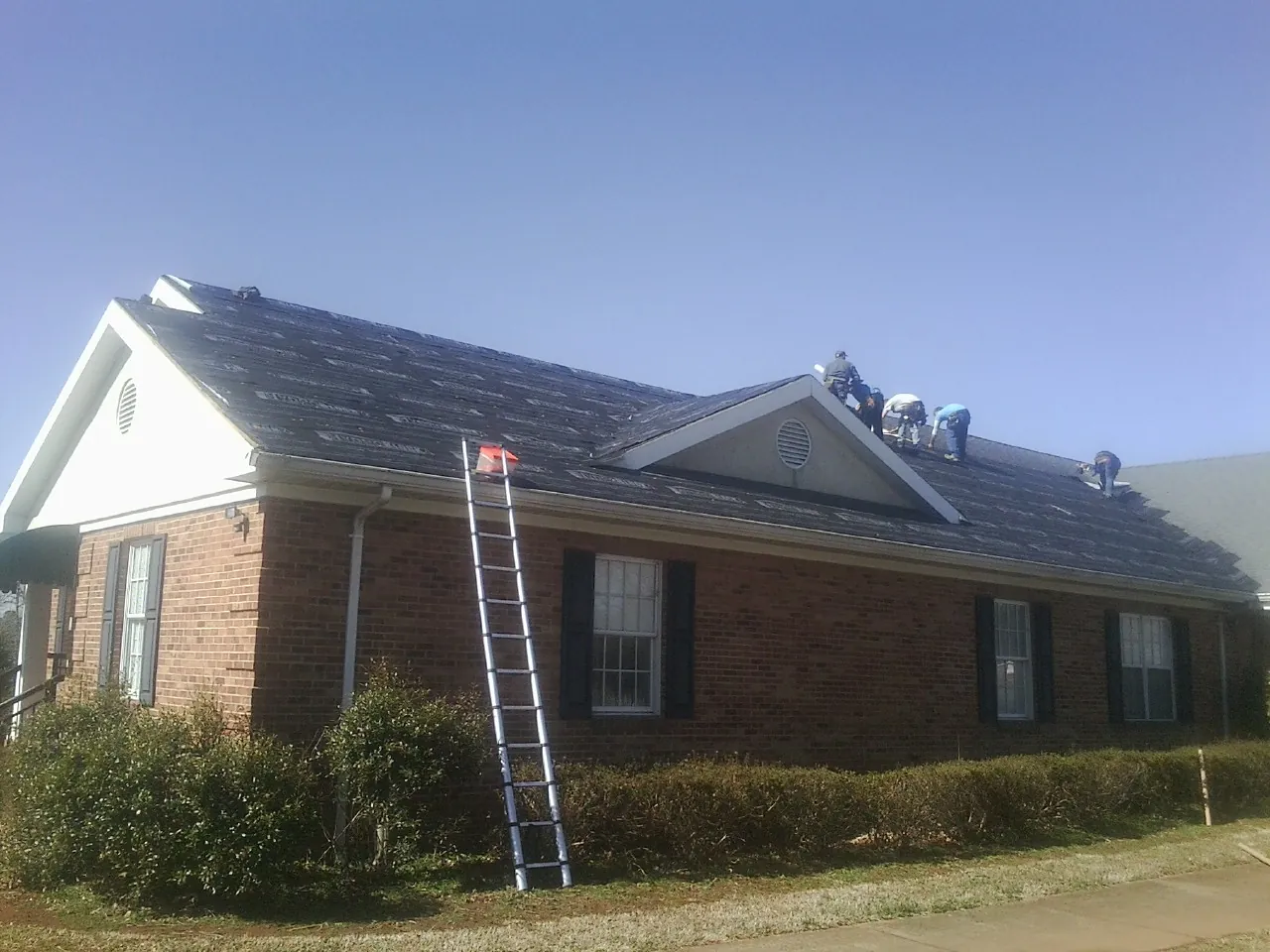 Crew tearing shingles off a brick ranch roof with a ladder set — Metal Roof Repair work by our crew in Camarillo