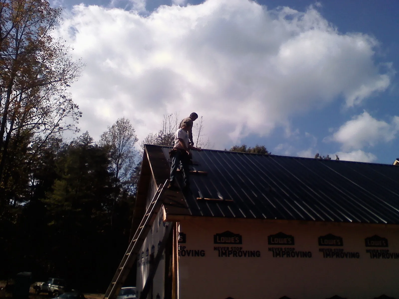 Roofer fastening dark metal panels high against a cloudy sky, from a Roof Inspection job in Camarillo